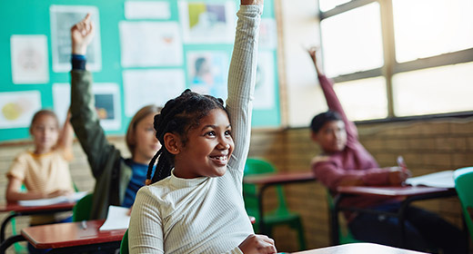 Young child in a classroom raising her hand to answer a question