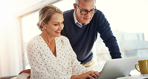 Older couple sitting at their kitchen counter looking at a laptop
