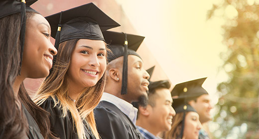 College graduates in cap and gown standing in a line while one of the girls smiles at the camera