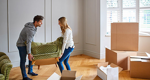 Young couple lifting a small couch in their newly purchased home sorrounded by moving boxes