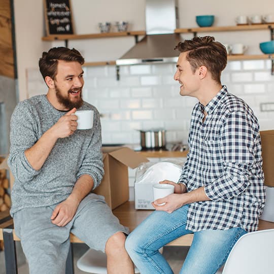 male couple taking a break from unpacking moving boxes at their home by drinking coffee and chatting