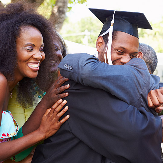 Family congratulating and hugging their son who is in a graduation cap and gown