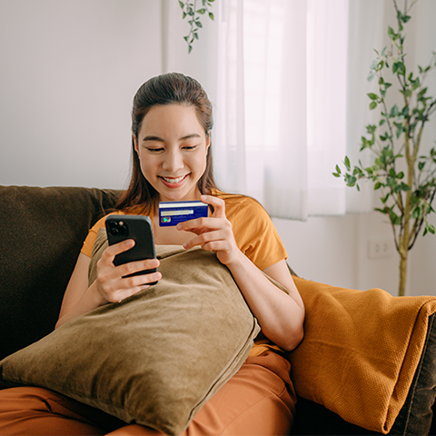 woman sitting on her couch holding her phone and wings card
