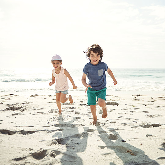 Two kids in shorts and t shirts running on a beach