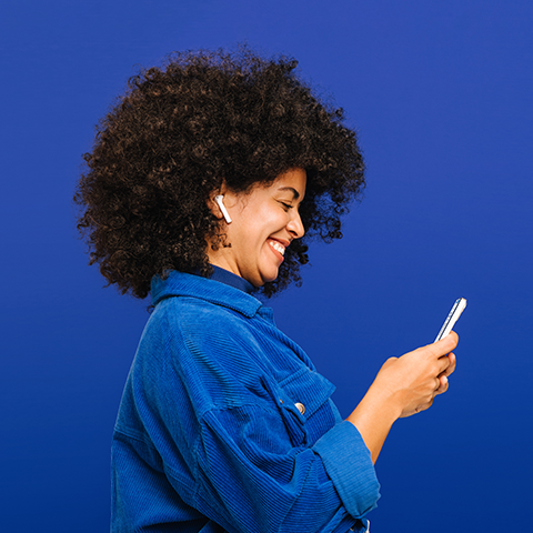 woman in blue corduroy jacket smiling while holding her phone_480x480
