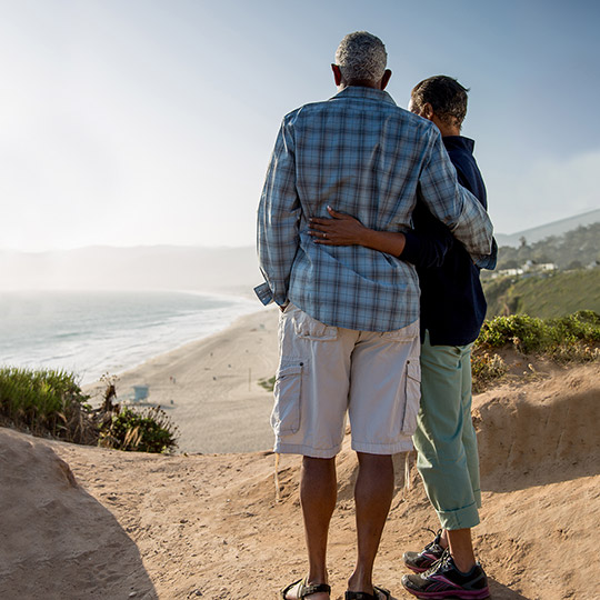 Older couple standing together overlooking a beach and the ocean during a sunny day