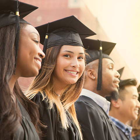 College graduates in cap and gown standing in a line while one of the girls smiles at the camera