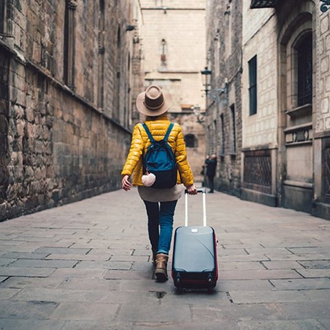 /getmedia/e6af7b52 3618 48ec a4e8 e7f52315a1bf/Woman walking down a cobblestone alley while rolling a suitcase