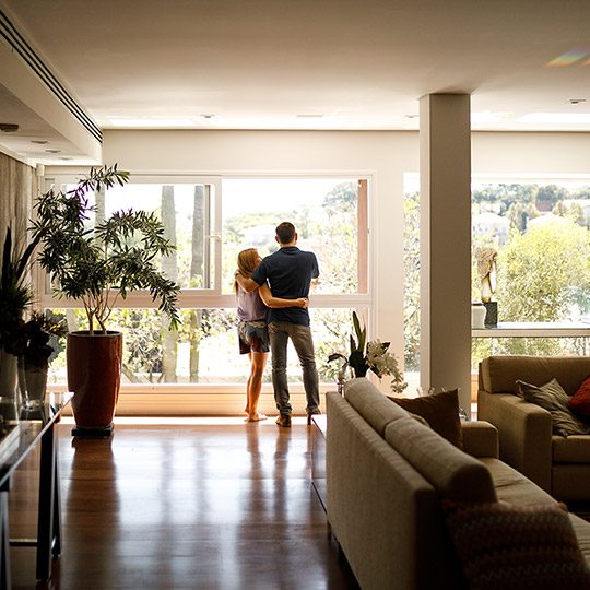 Couple standing arm in arm near a large window inside their family room