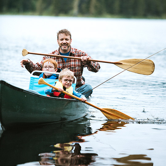 Father canoeing on a lake with his two young sons