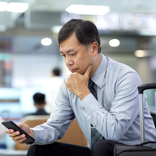 Man in a shirt and tie sitting at the airport with his luggage and staring intently at his mobile phone