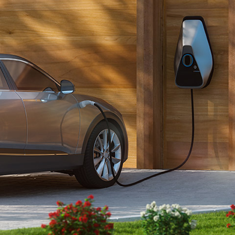 A high end electric car is being charged in front of a fancy house