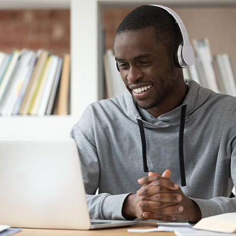 College age man sitting at a table wearing headphones and looking at a laptop