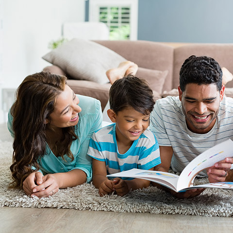 Family of four reading a book together on the living room carpet