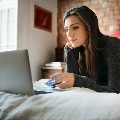 Girl laying on a bed preparing to type her credit card number into her laptop for an online purchase