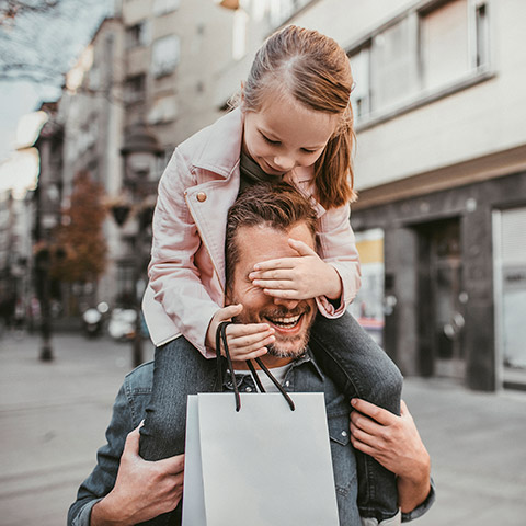 Little girl riding piggyback on her father while holding a shopping bag after leaving a store