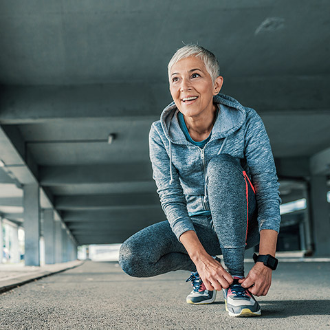 Older woman in running attire stopping to kneel down and tie her shoes
