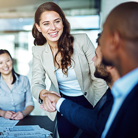 Woman shaking the hand of a client while others at the conference table look on
