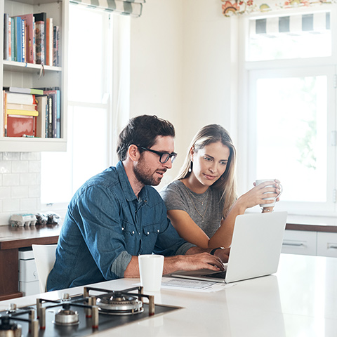 Young couple sitting at their kitchen island looking at a laptop