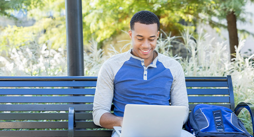 student sitting on a bench with their laptop 520x280